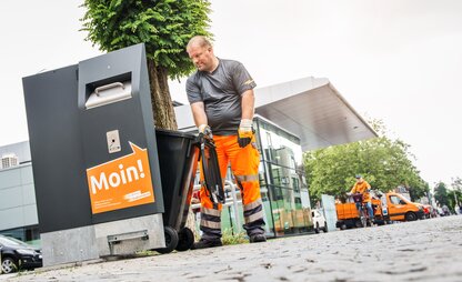 Auf einer belebten Straße leert ein Mitarbeiter einen öffentlichen Müllbehälter. | © Die Bremer Stadtreinigung