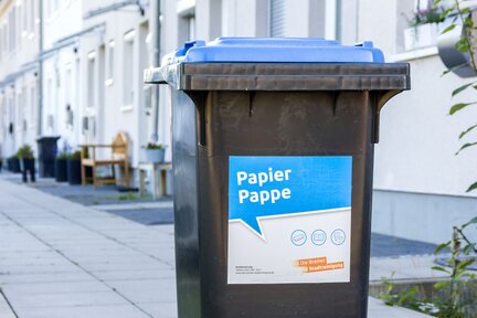 Eine Papiertonne mit blauem Deckel, die vor einer Hausreihe steht. Auf der Tonne steht " Papier, Pappe". | © Die Bremer Stadtreinigung