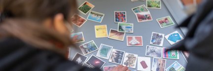 Zwei Frauen beugen sich über verschiedene Fotos, die technische Gegenstände, Landschaften und Gebrauchsgegenstände zeigen. | © Die Bremer Stadtreinigung