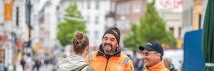Zwei Angestellte von DBS beraten eine Bürgerin in einer belebten Straße. | © Die Bremer Stadtreinigung