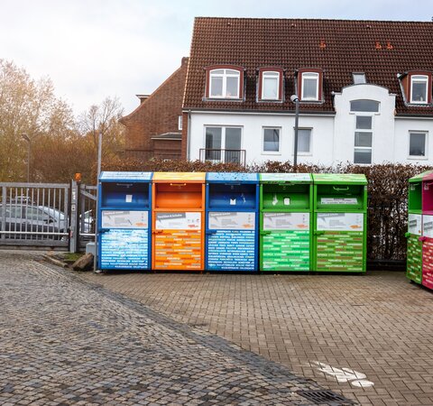 Acht Container in unterschiedlichen Farben für Textilien und Schuhe, die auf einem kleinen Hof vor einem Haus stehen. | © Die Bremer Stadtreinigung