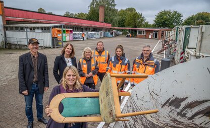 Maike Schaefer entsorgt einen Stuhl an der Modern-Station Kirchhuchting. Im Hintergrund sind DBS-Mitarbeitende und Daniela Enslein zu sehen. | © Die Bremer Stadtreinigung