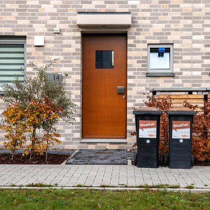 Frontalansicht eines Hauseingangs mit zwei Biotonnen, die am Gehweg bereitgestellt wurden. | © Die Bremer Stadtreinigung