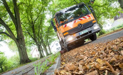 In der Froschperspektive ist ein Straßenreinigungsfahrzeug zu sehen, das in einer Allee Laub entfernt. | © Die Bremer Stadtreinigung