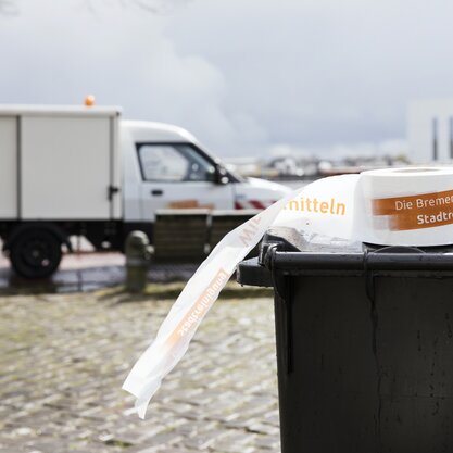 Absperrband des Kontrolldiensts auf einer Tonne | © Die Bremer Stadtreinigung Ein Absperrband des Kontrolldiensts liegt auf einer Restmülltonne. Im Hintergrund ist das Fahrzeug des Kontrolldiensts zu sehen, das illegale Müllablagerungen untersucht. | © Die Bremer Stadtreinigung