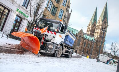 Ein Räumungsfahrzeug mit Schneeschippe des Winterdients fährt in Richtung der Haltestelle Schüsselkorb. Im Hintergrund ist der Bremer Dom zu sehen. | © Die Bremer Stadtreinigung