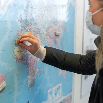 Eine junge Frau steht vor einer Weltkarte der Tour Global und verschiebt einen Magneten darauf. | © Die Bremer Stadtreinigung