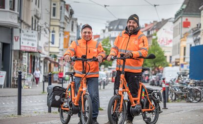 Ein DBS-Beratungsteam auf der Straße mit zwei orangenen Fahrrädern. | © Die Bremer Stadtreinigung