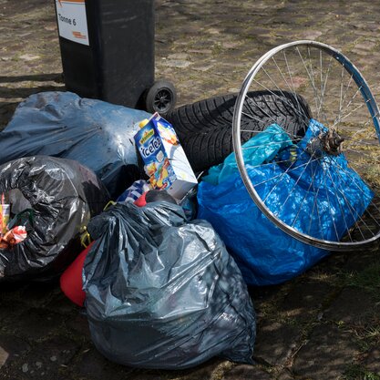 Illegale Müllablagerungen auf der Straße | © Die Bremer Stadtreinigung Vor einer Mülltonne sind illegale Müllablagerungen zu sehen: Mehrere Mülltüten, auf der eine Eisteetüte und die Speichen eines Fahrrads liegen. | © Die Bremer Stadtreinigung